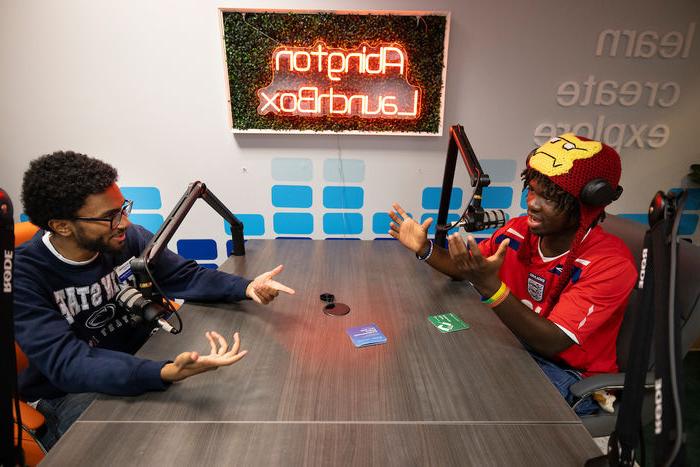 Two students during their podcast at a table with mics